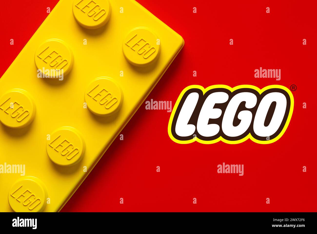 Nahaufnahme eines großen gelben lego-Blocks mit dem Lego-Logo auf rotem Hintergrund. Illustrativer Leitartikel Stockfoto