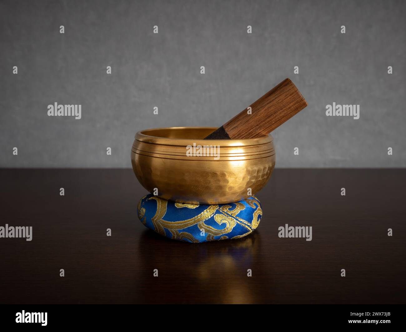 Eine goldene tibetische Klangschale mit Stürmer innen, die auf einem Ringkissen in der Mitte steht und auf einem unscharfen, sauberen Hintergrund isoliert ist Stockfoto