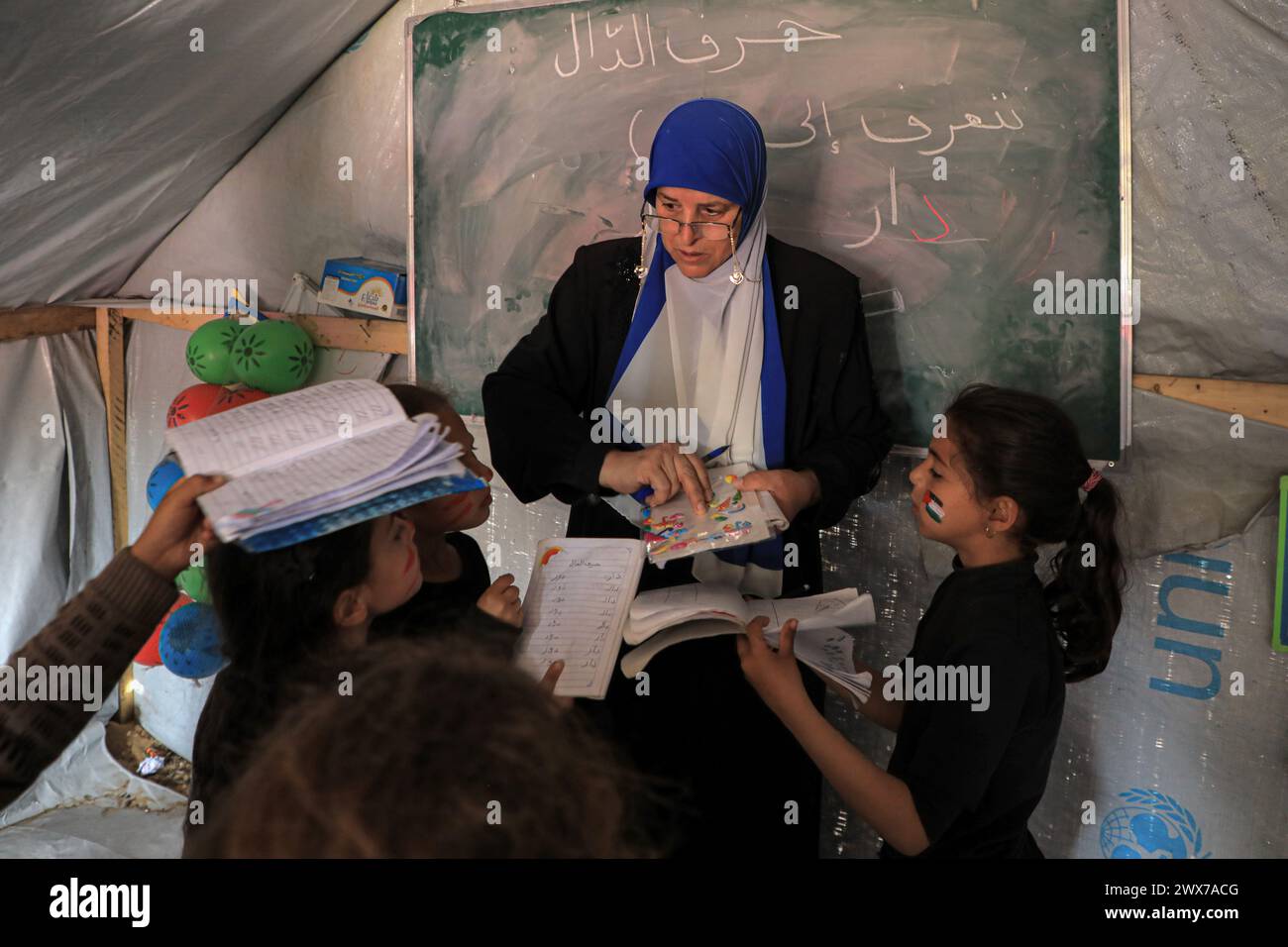 (240328) -- RAFAH, 28. März 2024 (Xinhua) -- Ein palästinensischer Lehrer unterrichtet Kinder in einem temporären Klassenzimmer in Rafah im südlichen Gazastreifen am 27. März 2024. Die schwere Bombardierung von Gaza durch Israel hat zu "direkten Schlägen" auf 212 Schulen innerhalb der Enklave geführt, so eine Analyse, die am Mittwoch in Zusammenarbeit mit den Vereinten Nationen veröffentlicht wurde. Satellitenbilder haben gezeigt, dass seit Beginn des Konflikts am 7. Oktober 2023 mindestens 53 Schulen „vollständig zerstört“ wurden. (Foto: Rizek Abdeljawad/Xinhua) Stockfoto
