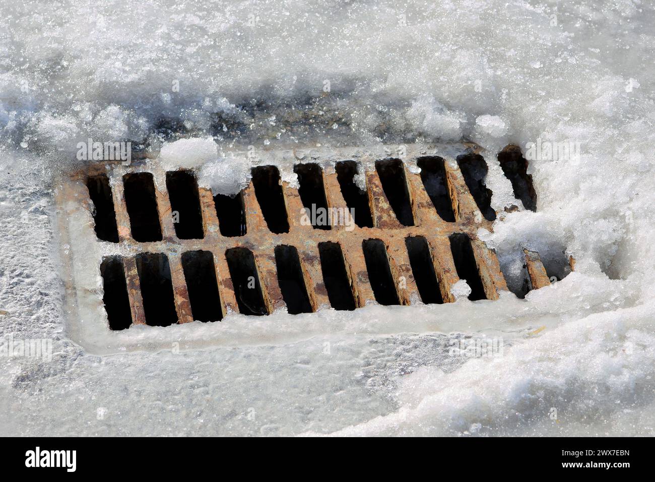 Rostiges Drainagegitter im Schnee auf der Straße. Der Beginn des Auftauens im Frühjahr. Stockfoto