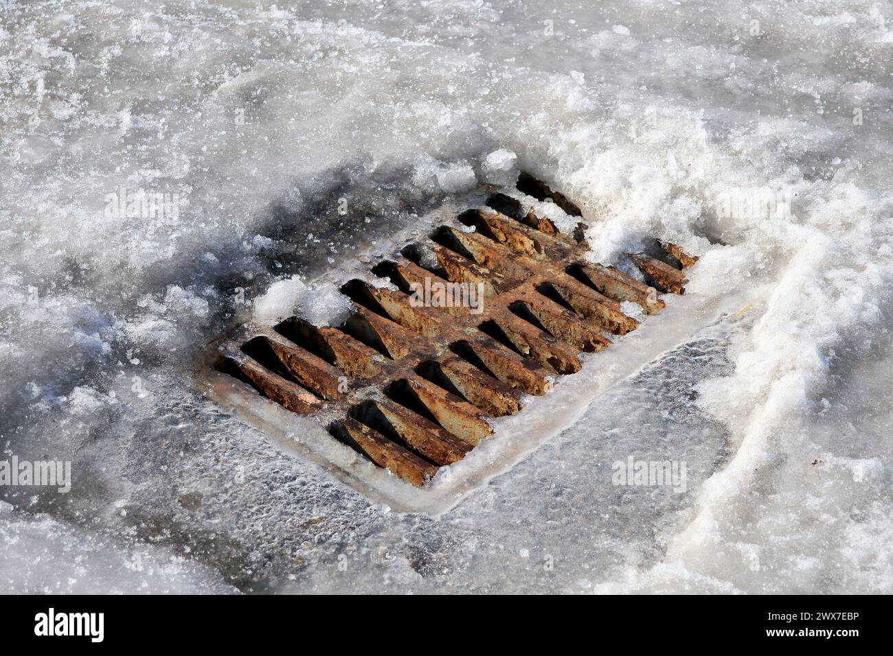 Rostiges Drainagegitter im Schnee auf der Straße. Der Beginn des Auftauens im Frühjahr. Stockfoto