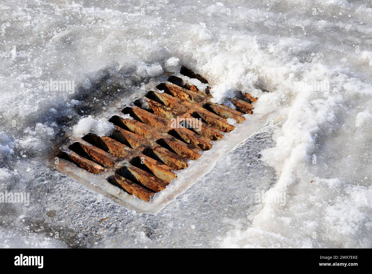 Rostiges Drainagegitter im Schnee auf der Straße. Der Beginn des Auftauens im Frühjahr. Stockfoto