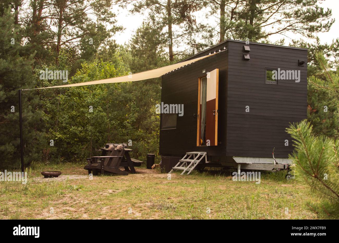 Eine modulare Rahmenwohnung auf Rädern, mit Holz vor dem Hintergrund eines Herbstwaldes gesäumt. Mobiler ökologischer Raum für Wohnen und Tourismus. Stockfoto