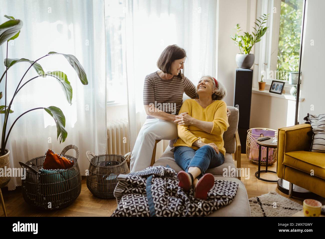 Lächelnde reife Frau, die Freizeit verbringt Schwiegermutter, die zu Hause im Wohnzimmer auf einem Stuhl sitzt Stockfoto