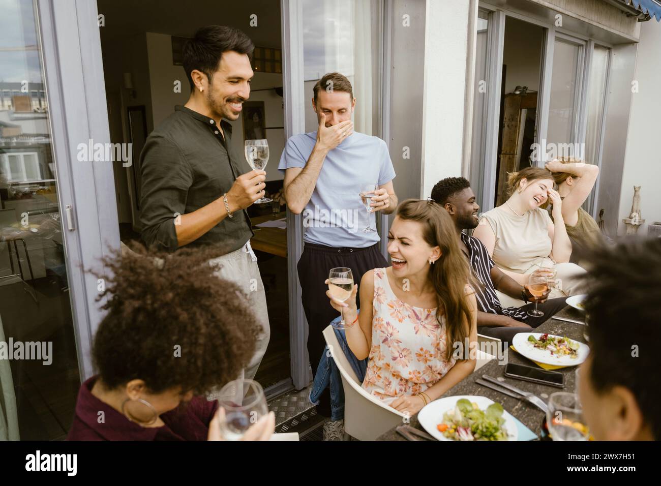 Eine Gruppe von männlichen und weiblichen multirassischen Freunden lacht beim Drink auf dem Balkon Stockfoto