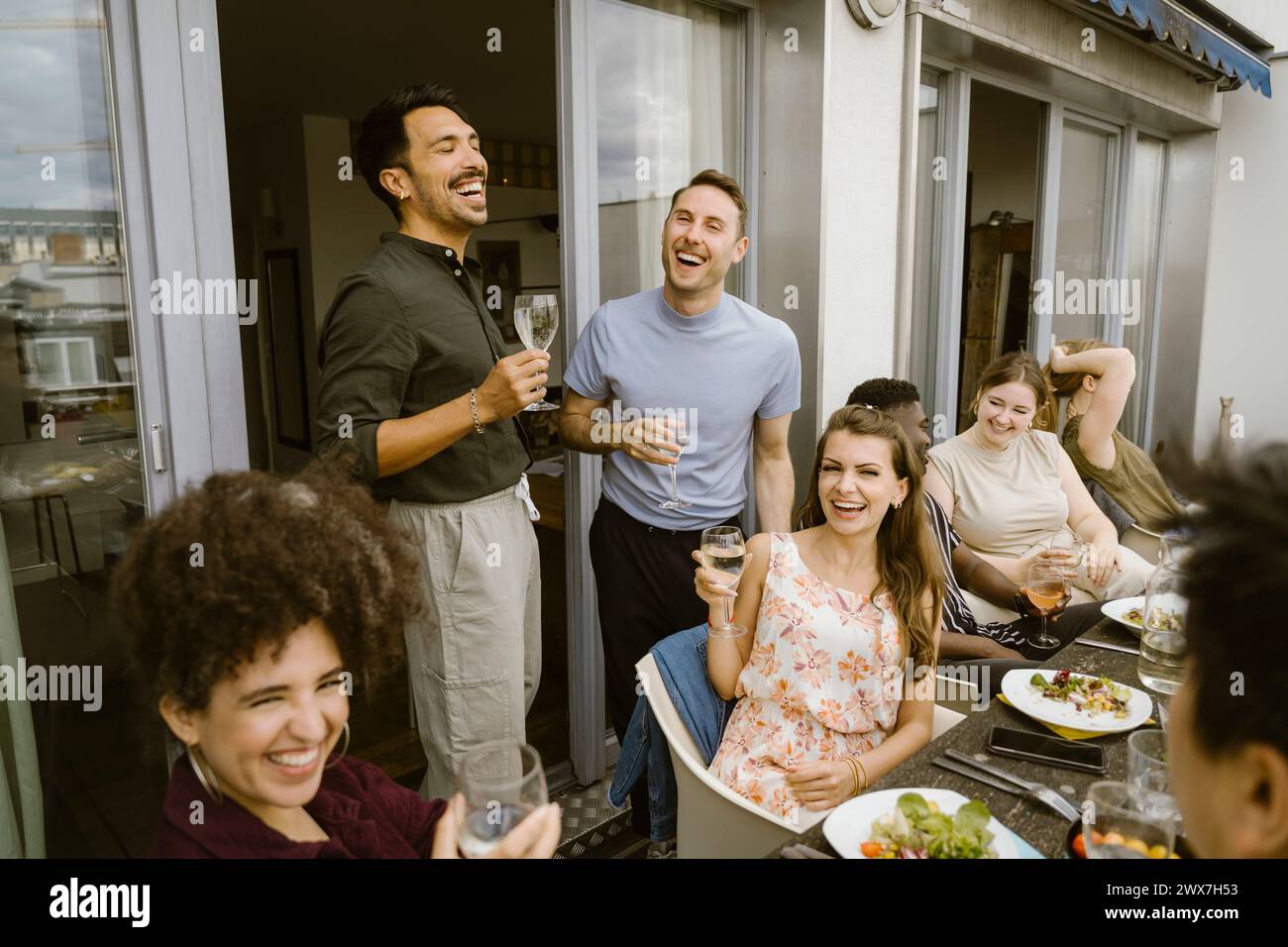 Eine Gruppe fröhlicher Freunde lacht, während sie eine Dinnerparty auf dem Balkon feiern Stockfoto