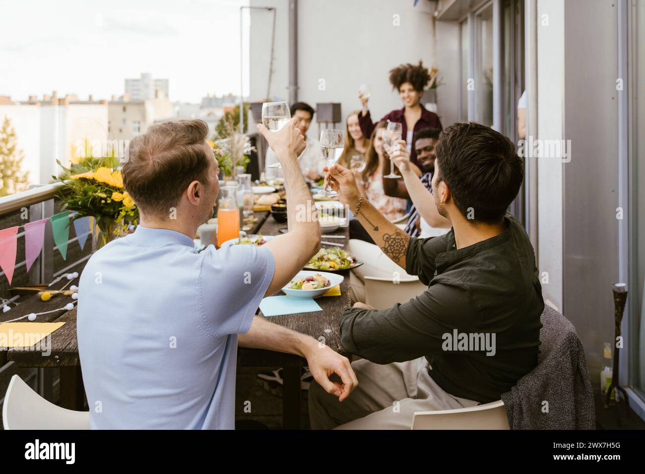 Männer, die Getränke trinken, mit einer Gruppe von Freunden, die am Esstisch auf dem Balkon sitzen Stockfoto
