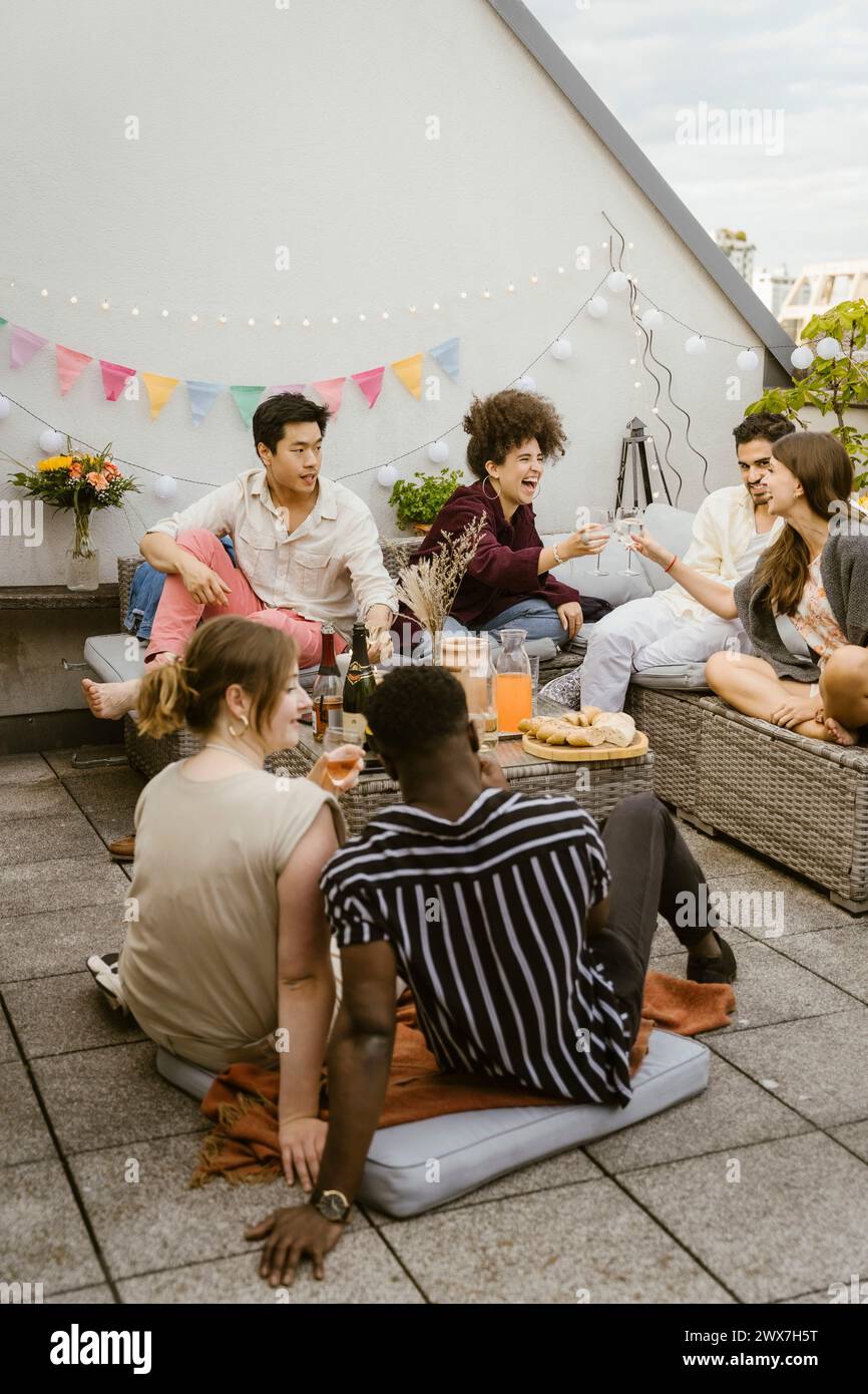 Eine Gruppe glücklicher multirassischer Freunde, die während der Party auf dem Balkon sitzen Stockfoto