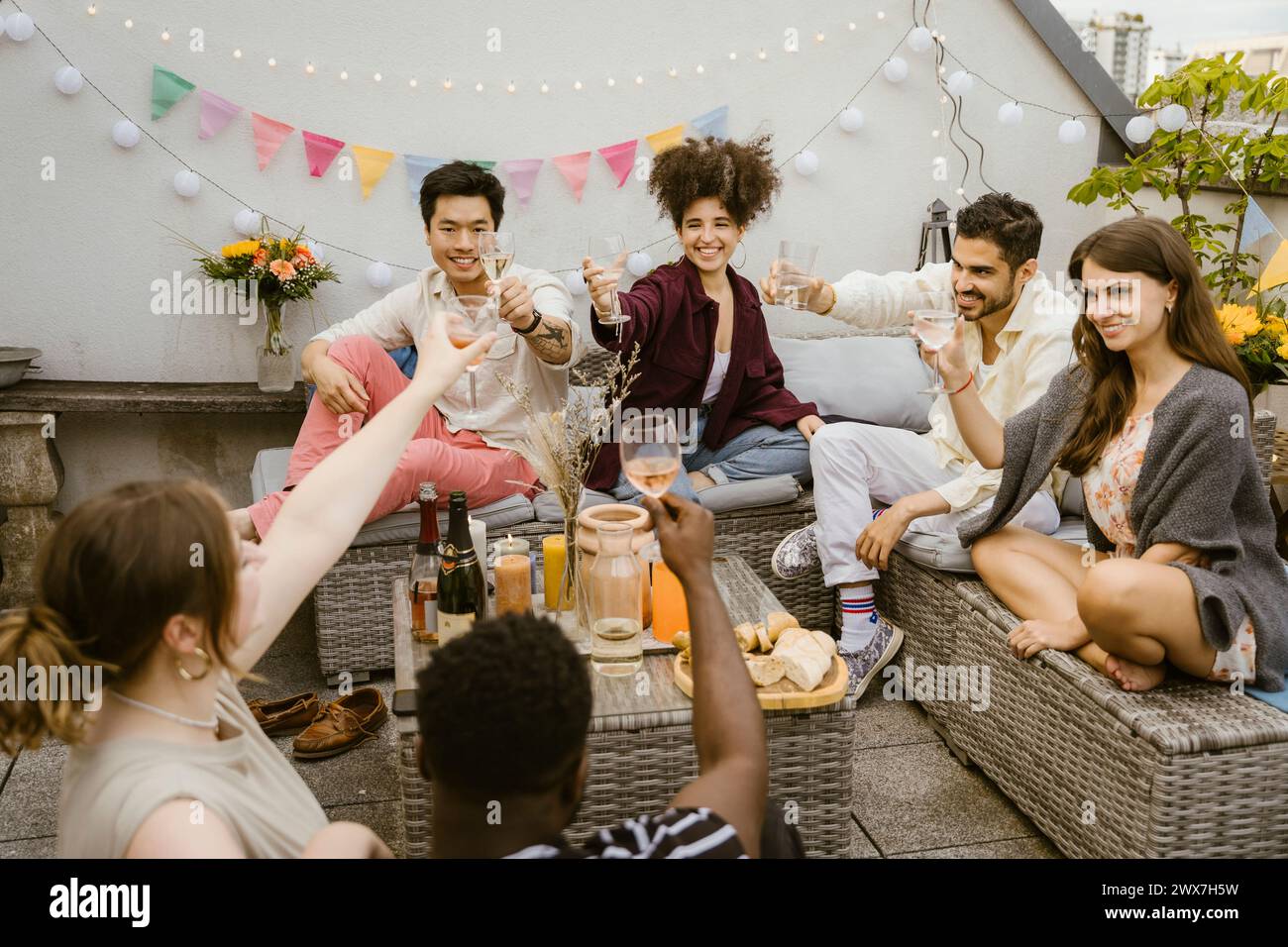 Gruppe von multirassischen Freunden, die zusammen auf dem Balkon sitzen und Getränke trinken Stockfoto