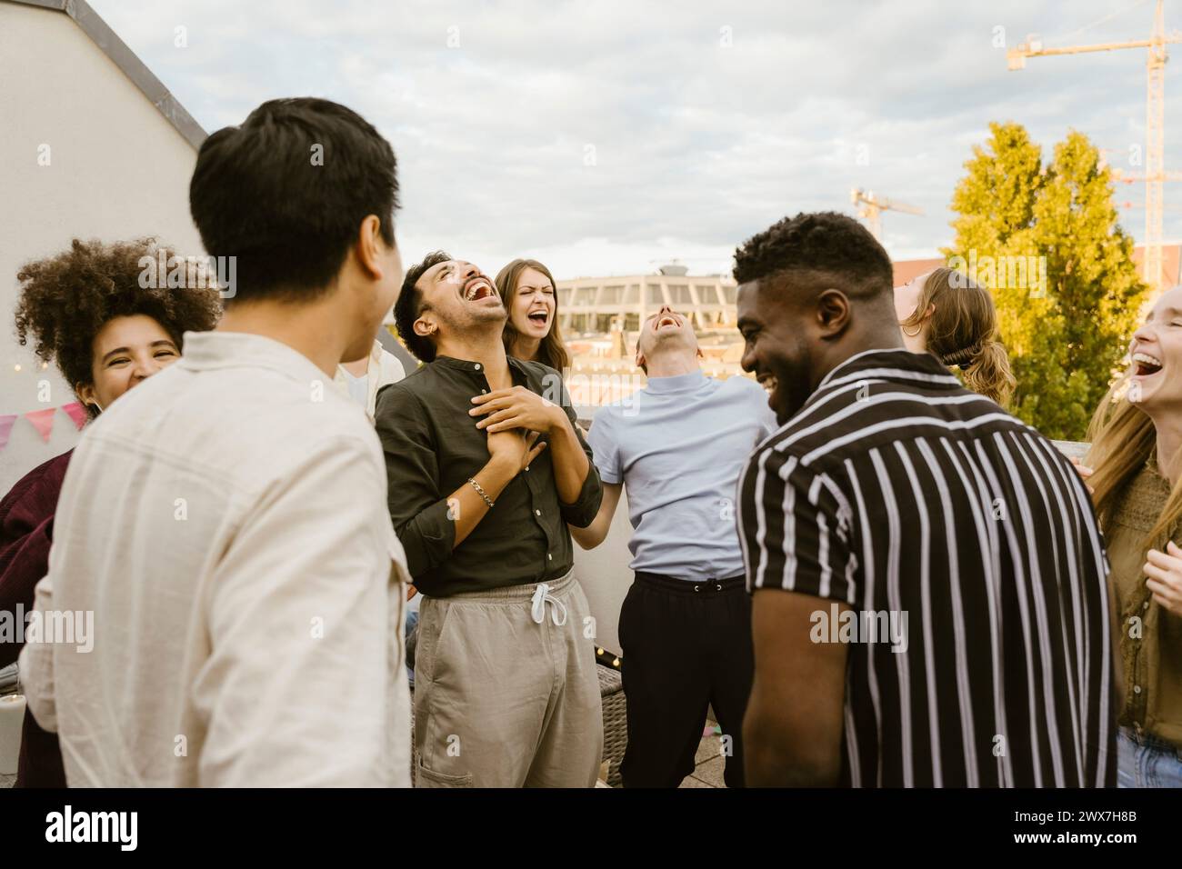 Eine Gruppe multirassischer männlicher und weiblicher Freunde lacht zusammen, während sie auf dem Balkon stehen Stockfoto