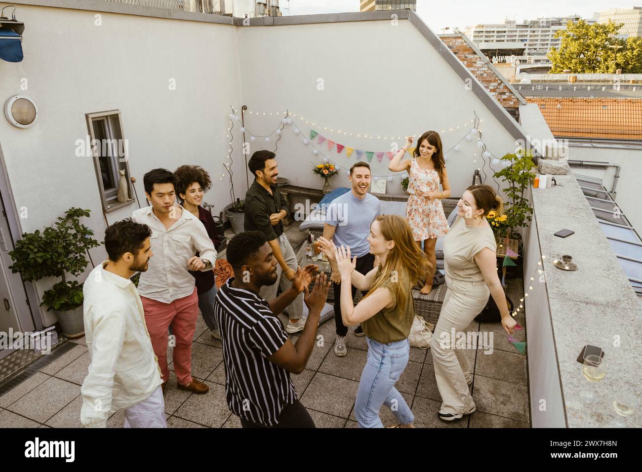 Gruppe sorgloser männlicher und weiblicher Freunde, die während des Abendessens auf dem Balkon tanzen Stockfoto