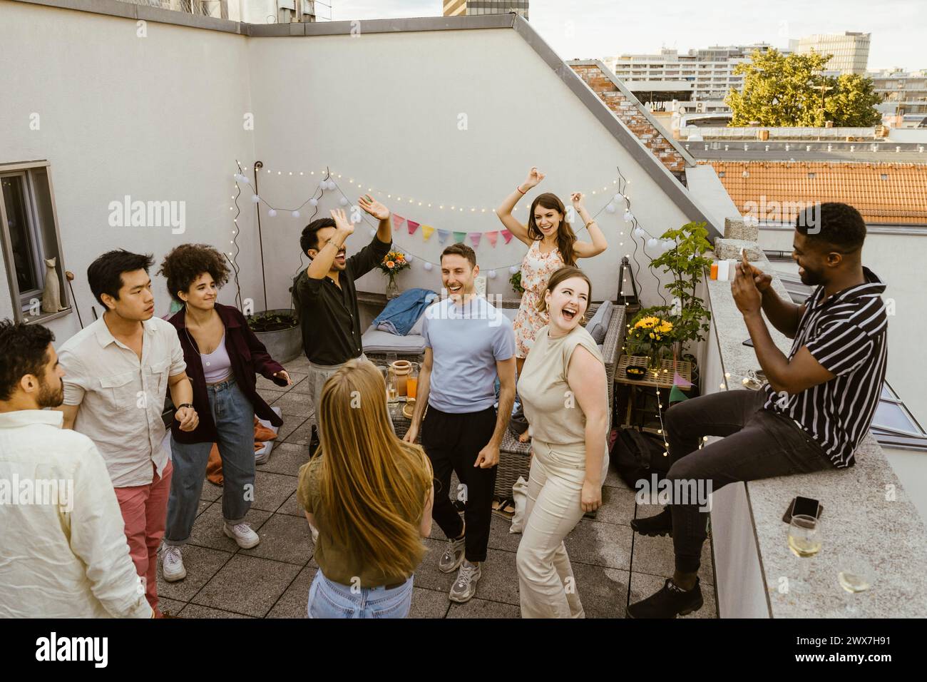 Ein Mann fotografiert eine Gruppe von Freunden, die auf einer Party auf dem Balkon tanzen Stockfoto