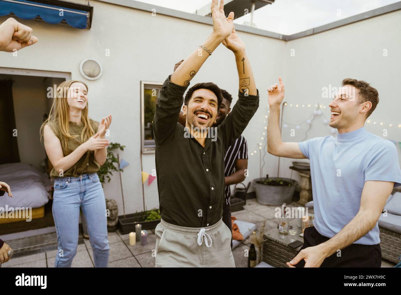 Fröhlicher Mann, der mit einer Gruppe von Freunden auf der Dachterrasse tanzt Stockfoto