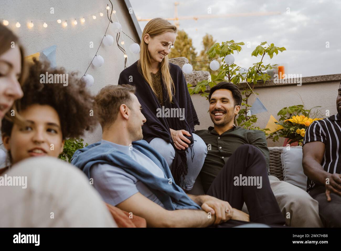 Gruppe männlicher und weiblicher Freunde, die sich unterhalten, während sie auf einer Party auf dem Balkon sitzen Stockfoto