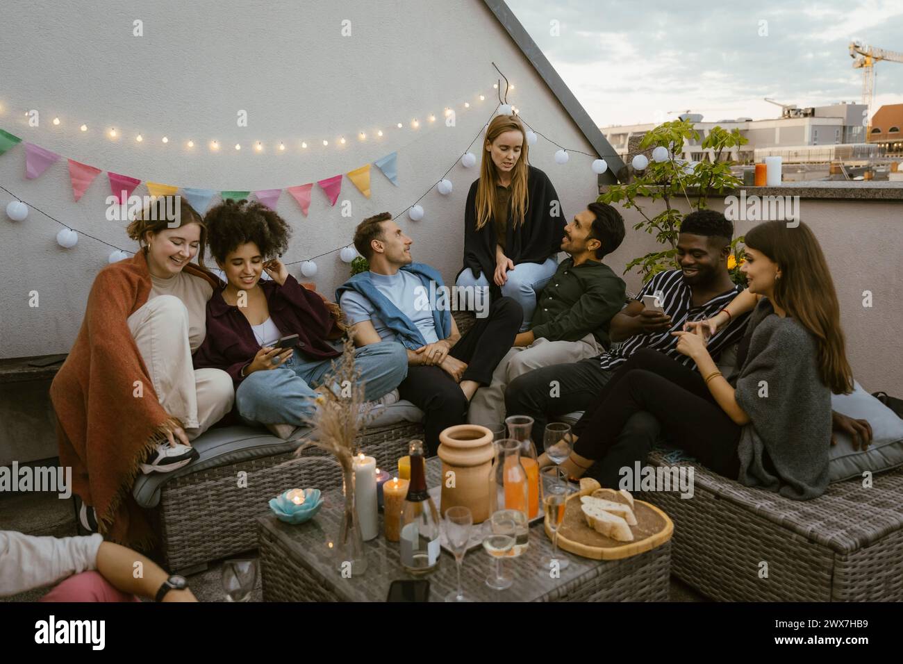Gruppe männlicher und weiblicher Freunde, die auf einer Party auf dem dekorierten Balkon sitzen und sich unterhalten Stockfoto