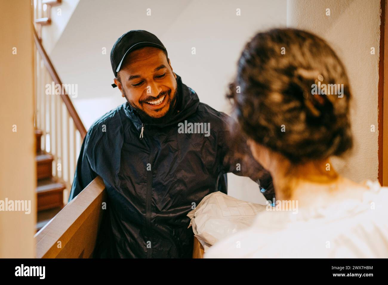 Ein lächelnder männlicher Zusteller, der das Paket an die Frau vor der Tür bringt Stockfoto