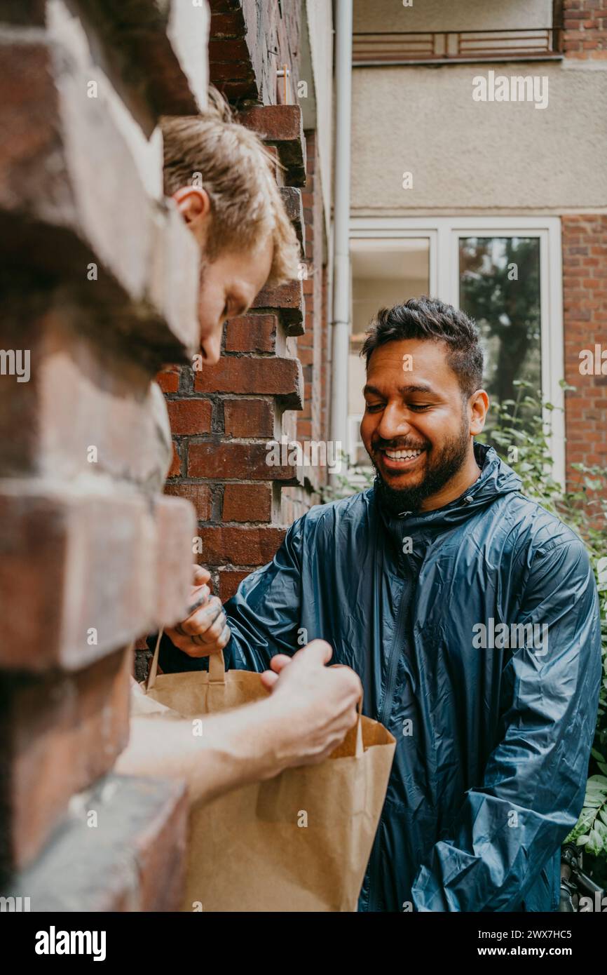 Lächelnder Zusteller, der das Paket vor der Haustür zustellt Stockfoto