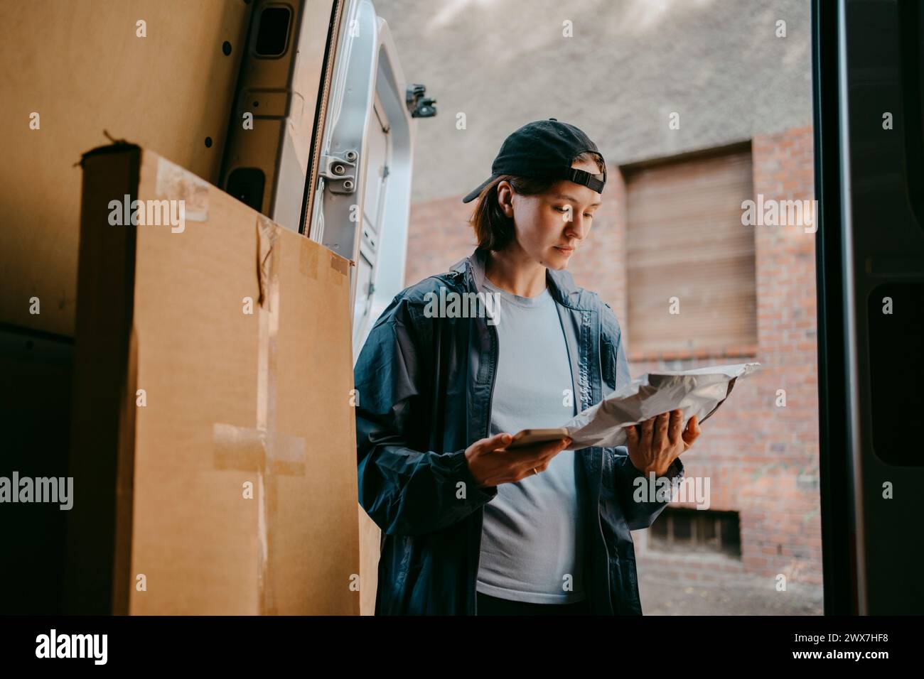 Weibliche Zustellperson untersucht das Paket, während sie in der Nähe des Transporters steht Stockfoto