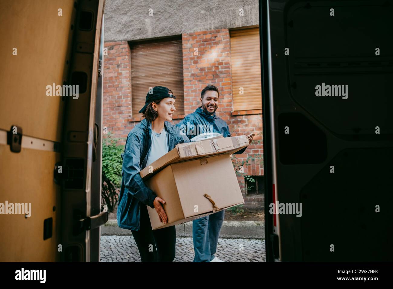 Männliche und weibliche Lieferkollegen mit Kisten aus dem Kofferraum Stockfoto