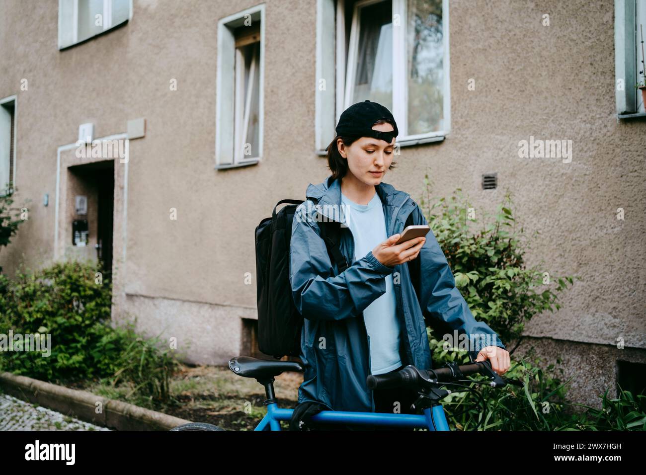 Weibliche Radfahrerin, die ihr Smartphone benutzt, während sie mit dem Fahrrad in der Nähe des Gebäudes steht Stockfoto