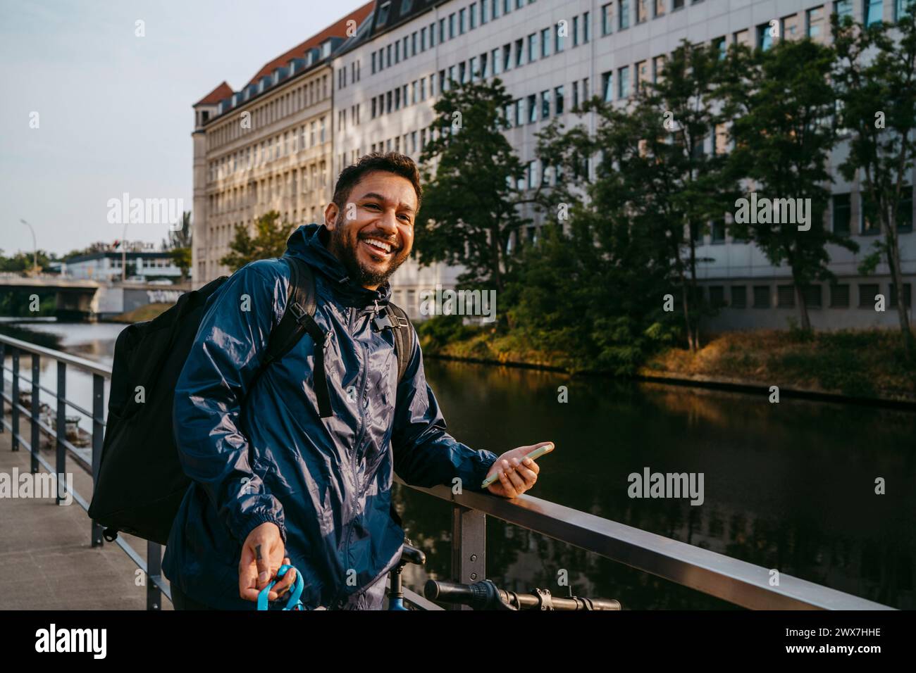 Glücklicher männlicher Essenslieferant, der neben dem Geländer am Kanal in der Stadt steht Stockfoto