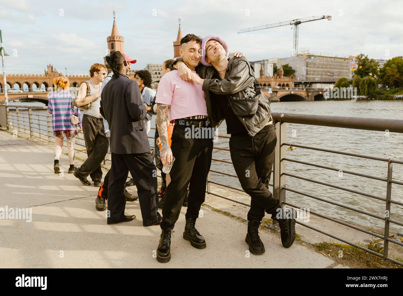 Schwuler Mann lehnt sich an einen nicht-binären Freund, der neben einem Geländer an der Promenade in der Stadt steht Stockfoto