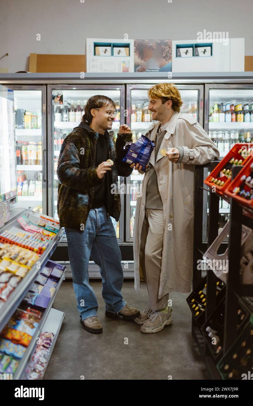 Glückliches Schwulenpaar, das sich mit einander unterhält, während er im Supermarkt Snacks trinkt Stockfoto