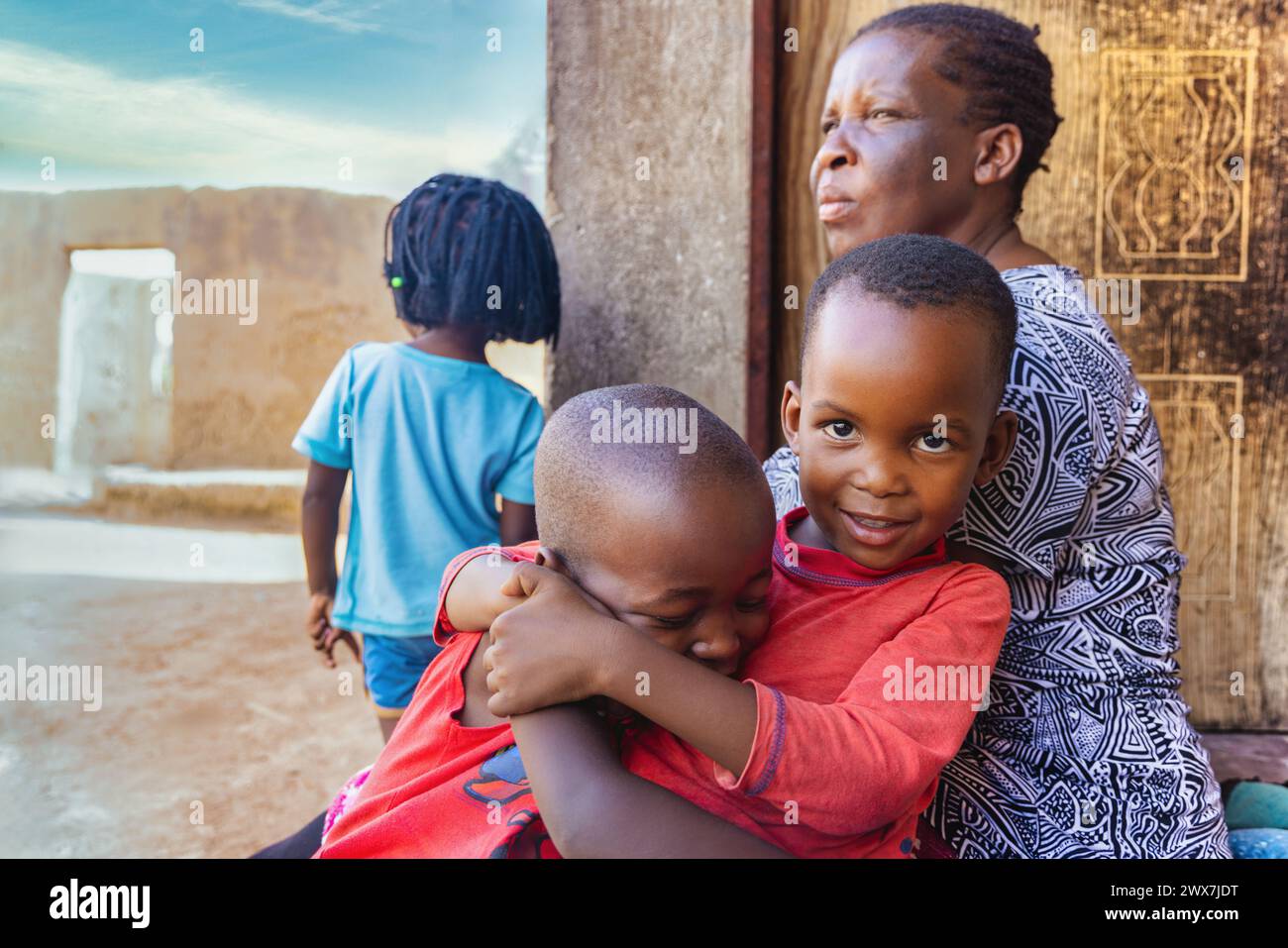 Nur wenige afrikanische Kinder spielen und streiten auf der Veranda vor dem Haus, Oma beobachtet, afrikanisches Dorfleben Stockfoto
