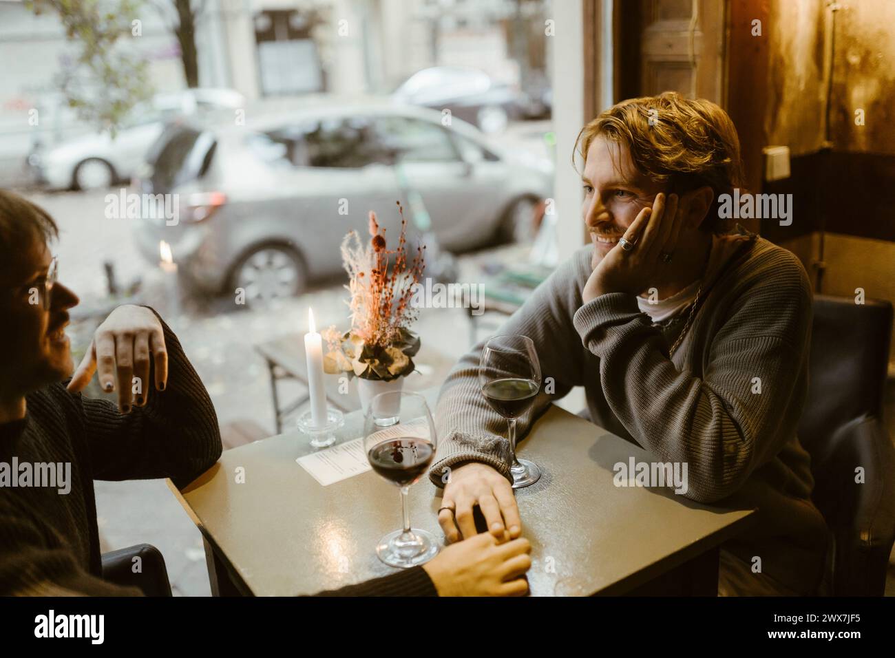 Lächelnder schwuler Mann, der sich auf den Ellenbogen stützt, während er mit einem Freund im Restaurant spricht Stockfoto