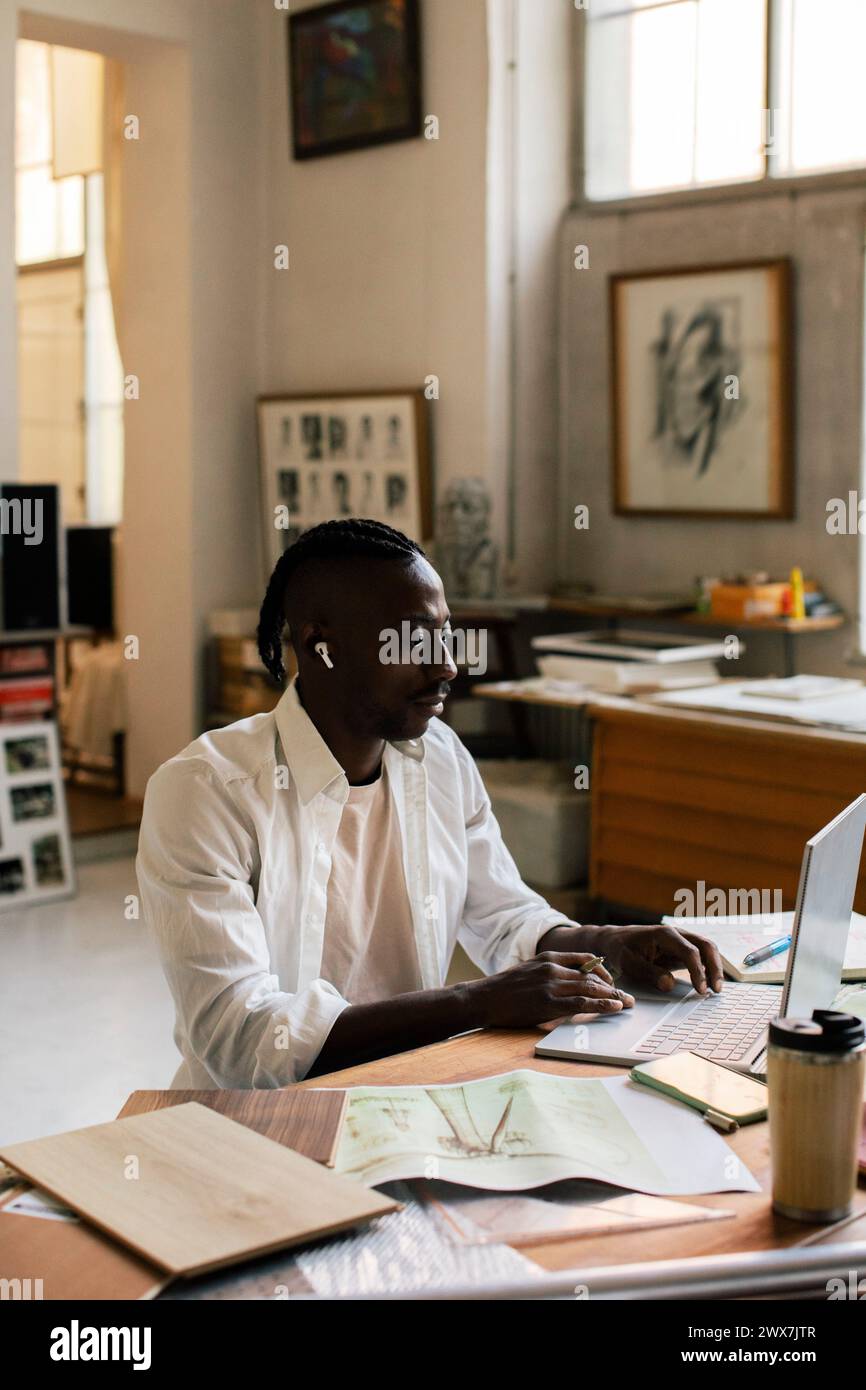 Männlicher Unternehmer, der am Laptop arbeitet, während er am Arbeitsplatz sitzt Stockfoto