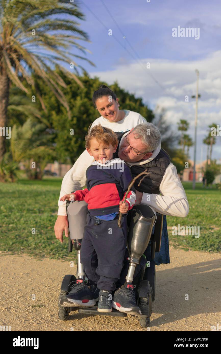 Mann im Rollstuhl und orthopädischen Beinen, genießt die Natur mit seiner Familie Stockfoto