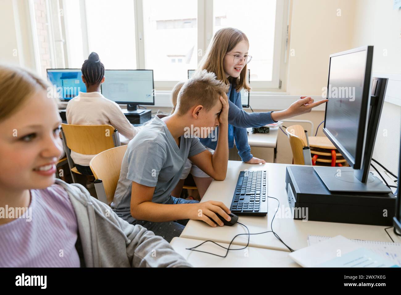 Mädchen, das auf den Bildschirm zeigt, mit einem männlichen Freund, der am Schreibtisch in der Schule sitzt Stockfoto