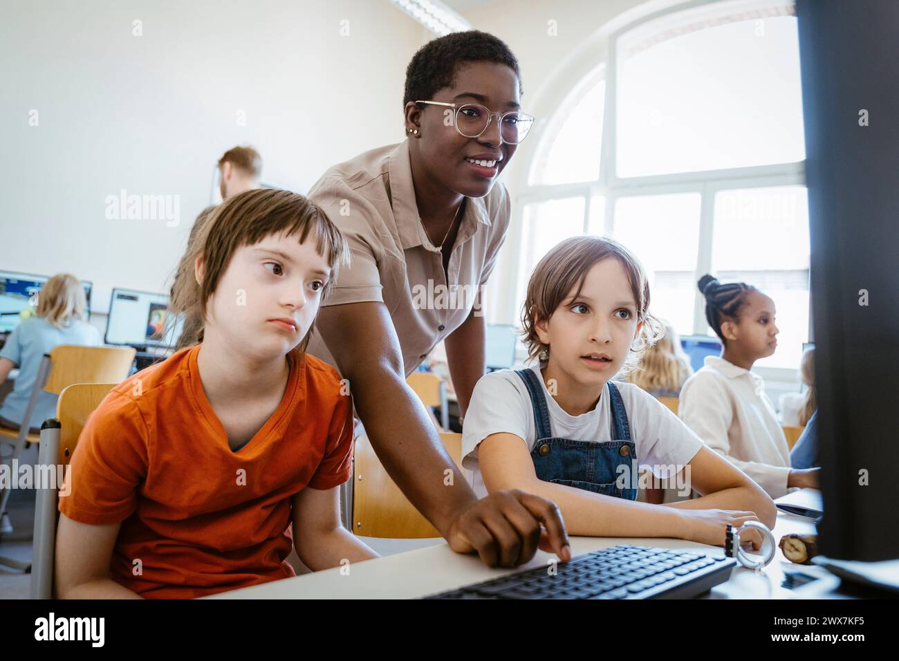 Lächelnde Lehrerin, die Mädchen mit Down-Syndrom im Computerunterricht in der Schule unterstützt Stockfoto