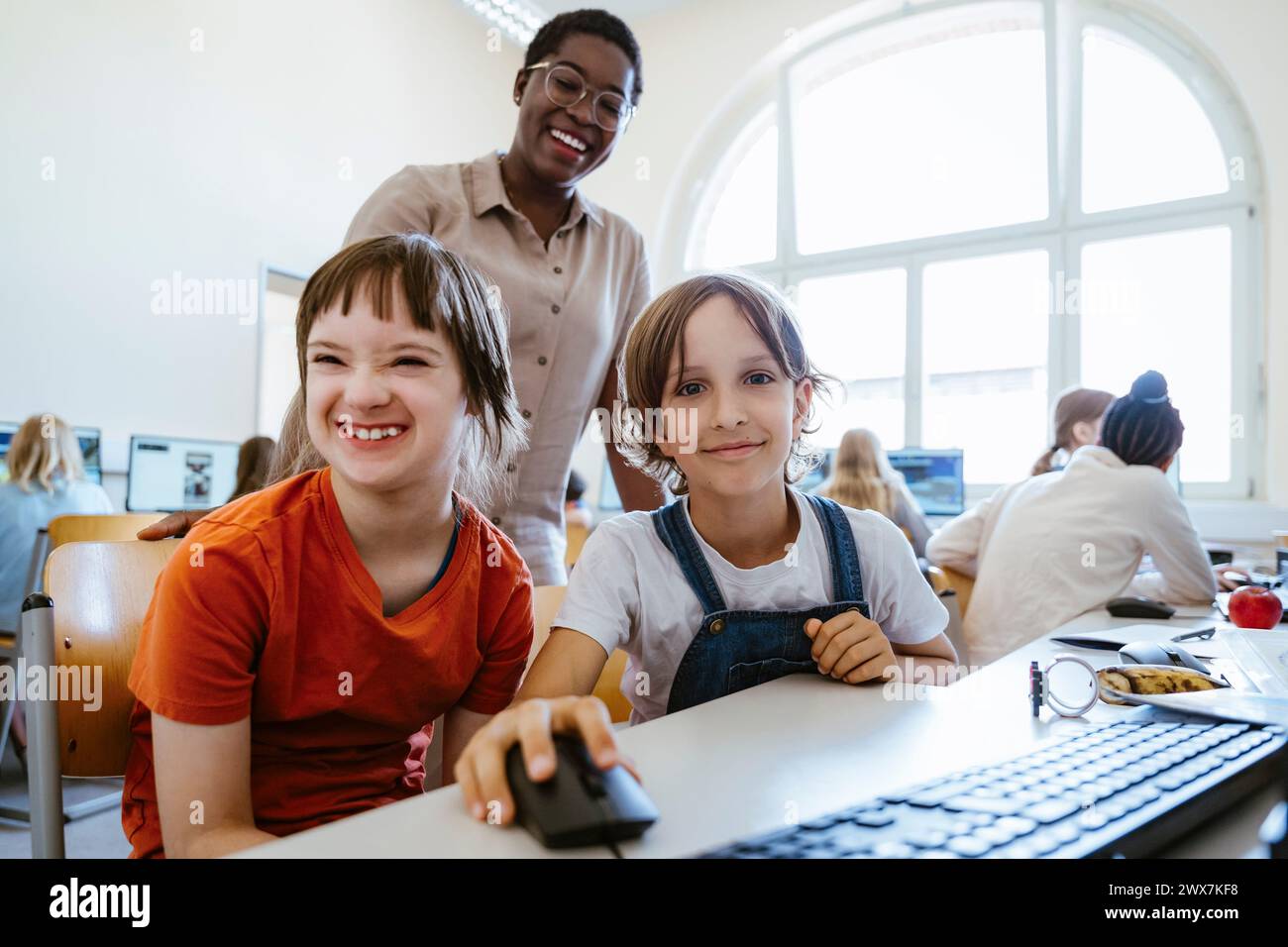 Porträt eines lächelnden Mädchens neben einer behinderten Freundin im Computerunterricht in der Schule Stockfoto