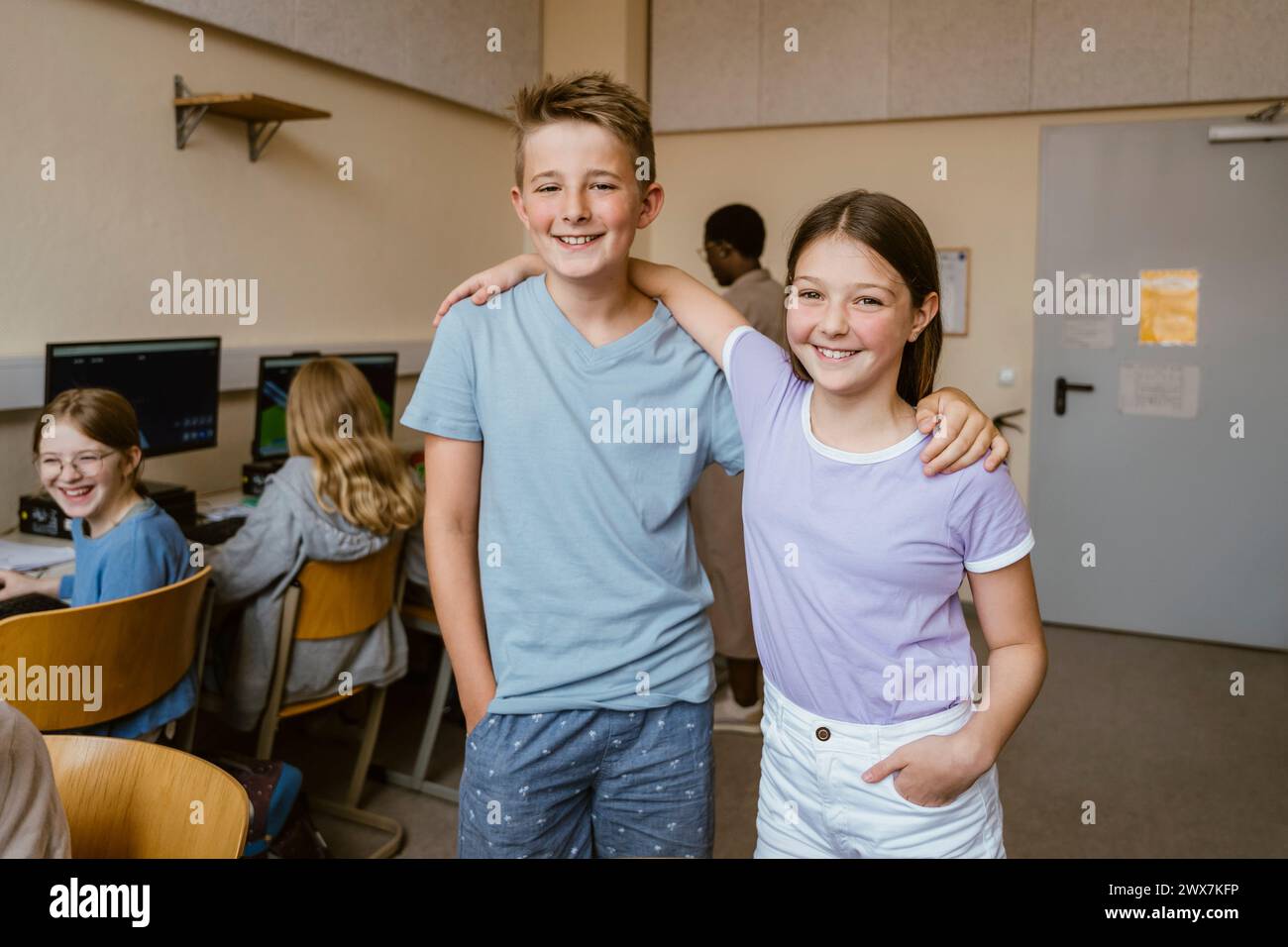 Porträt lächelnder männlicher und weiblicher Freunde, die mit Armen im Computerunterricht in der Schule stehen Stockfoto