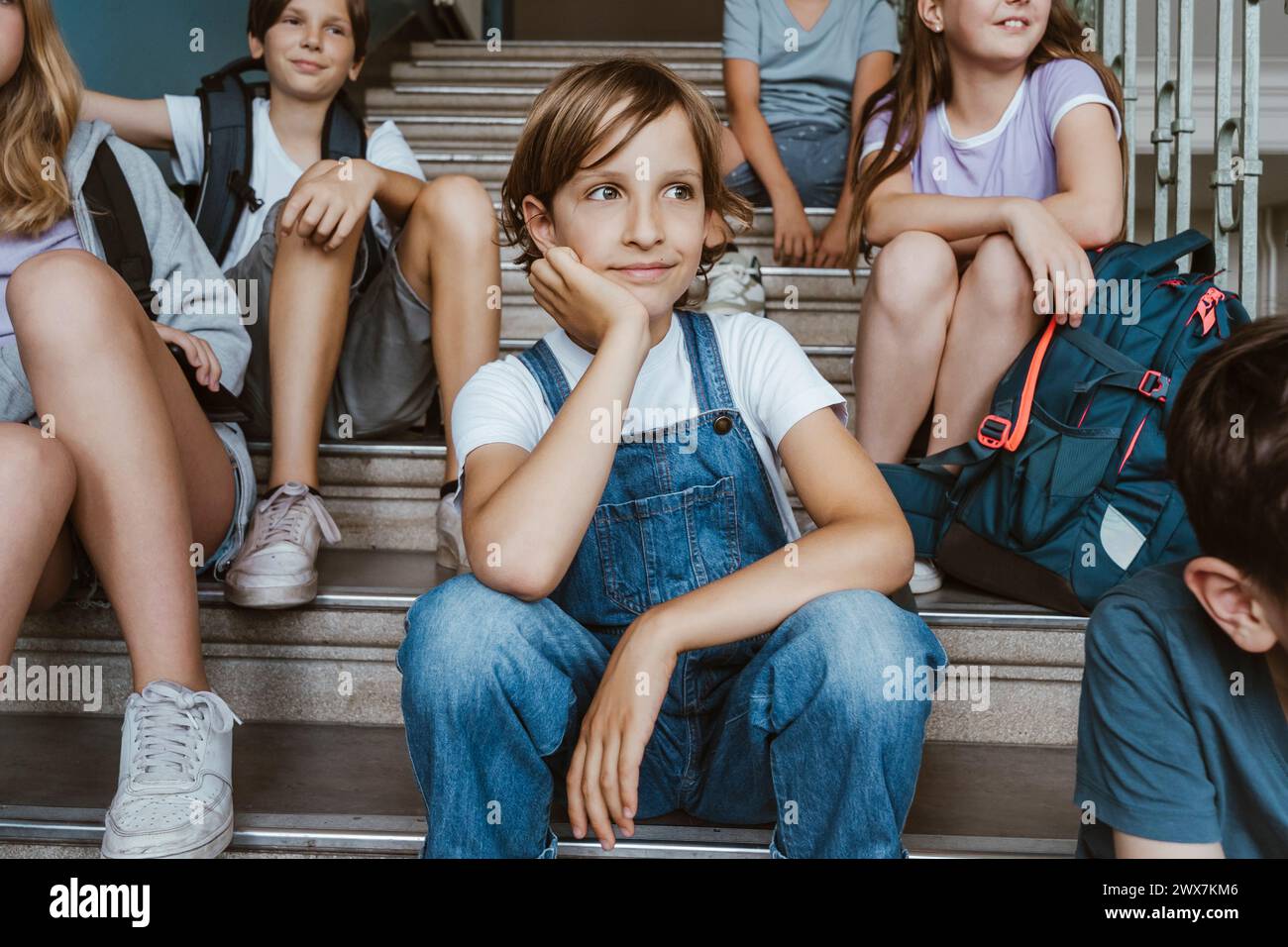 Ein nachdenkliches Mädchen, das sich auf den Ellenbogen lehnt, während er mit Freunden in der Schule auf der Treppe sitzt Stockfoto