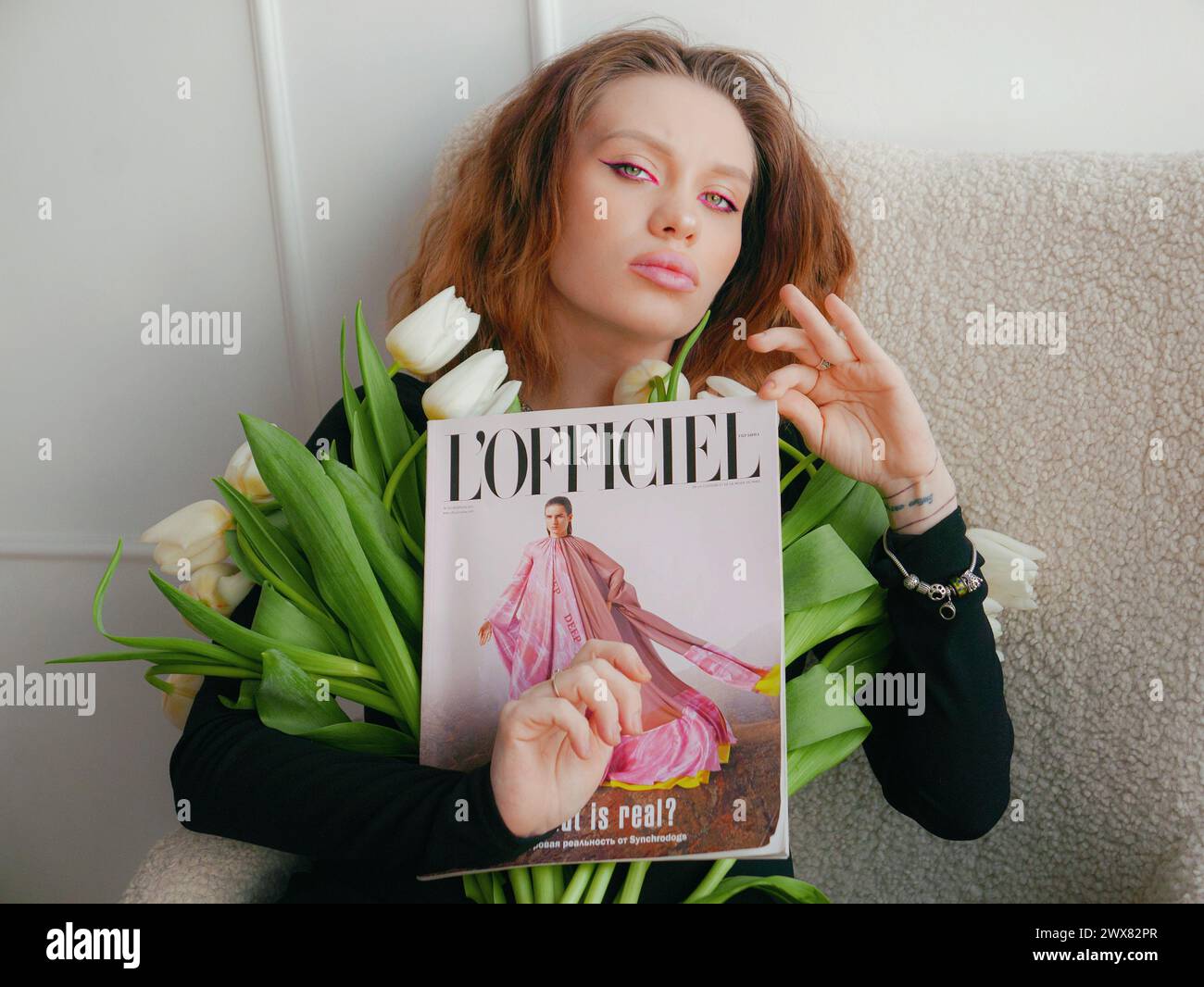 Eine Frau mit rosa Augen-Make-up in einem schwarzen engen Kleid mit weißen Tulpen Stockfoto