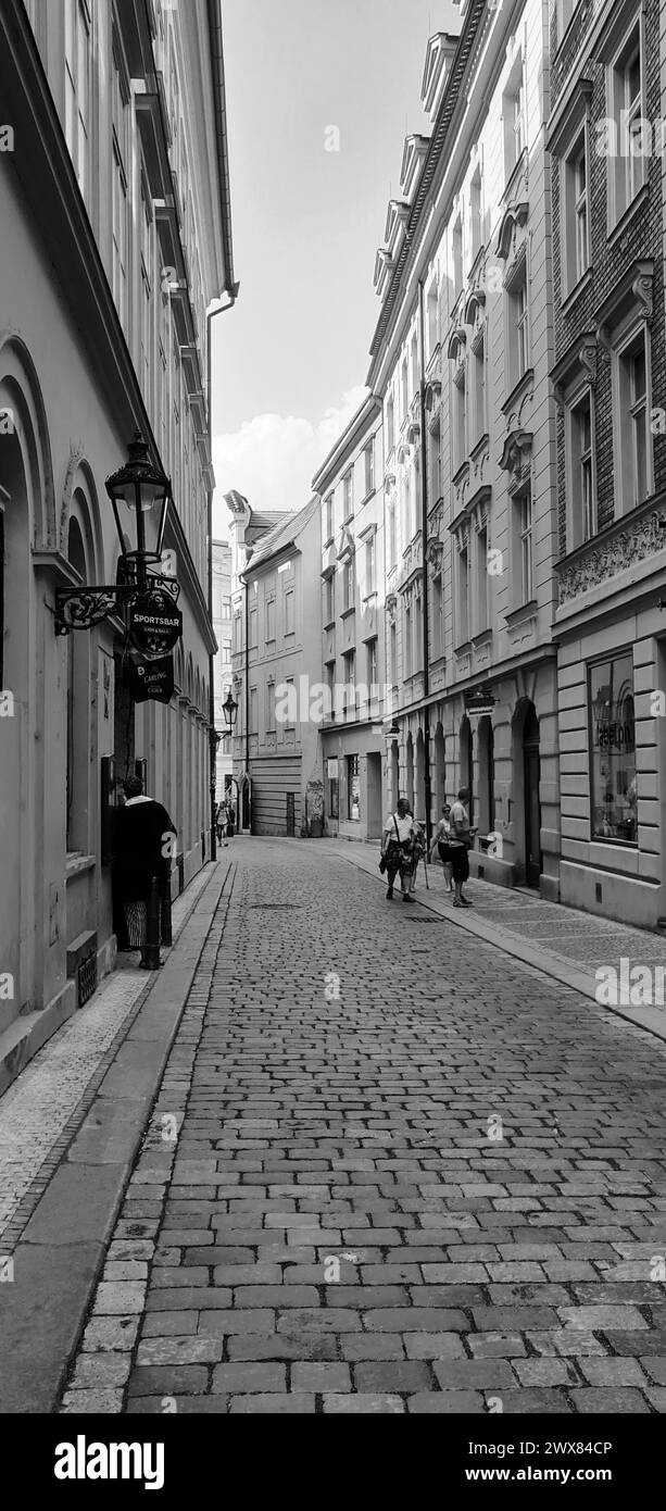 Eine Vertikal von Menschen, die auf einer engen Stadtstraße in Prag, Tschechien, in Graustufen spazieren Stockfoto