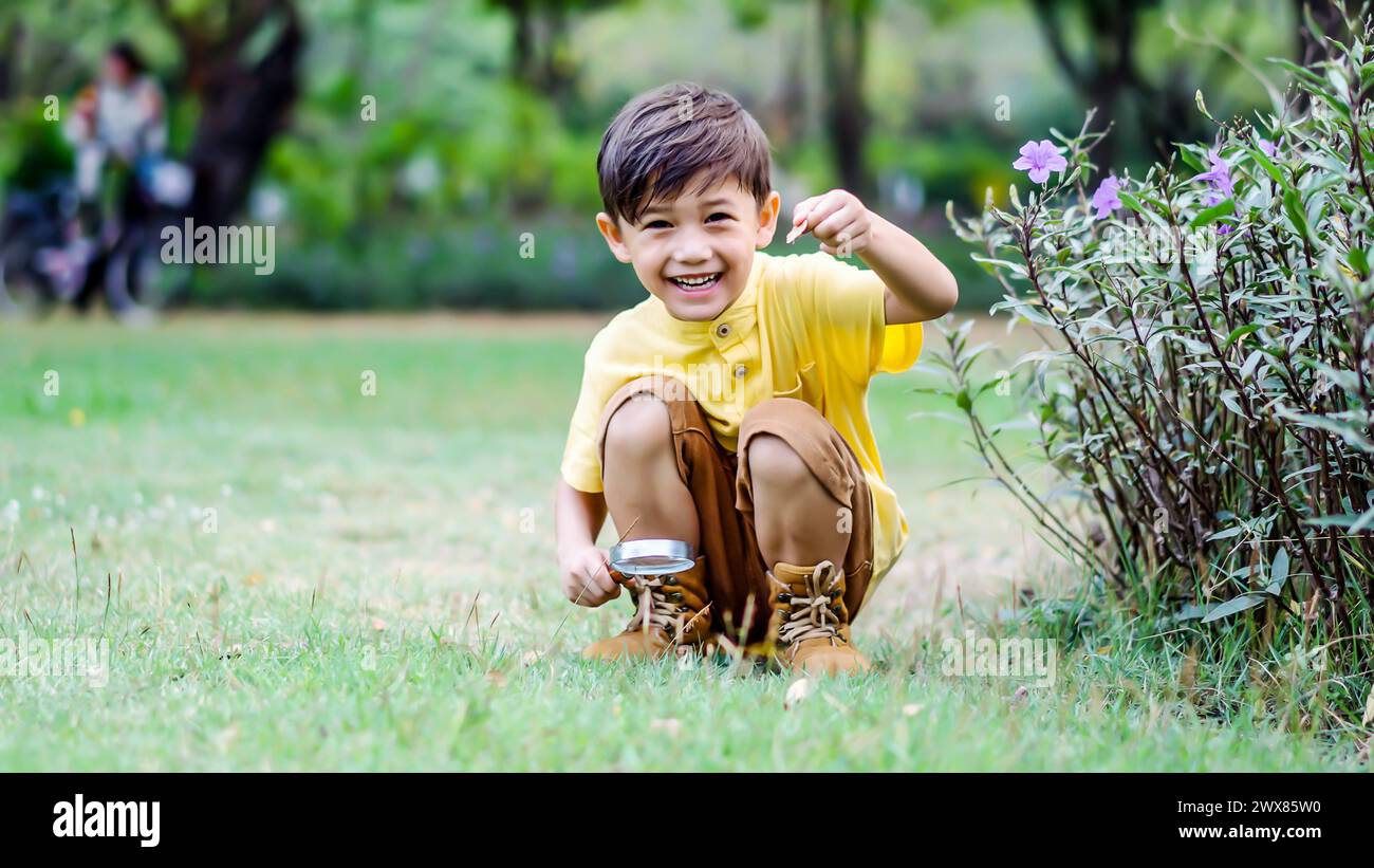 Ein kleiner Junge, der mit einer Tasse Bier auf Gras kniet Stockfoto