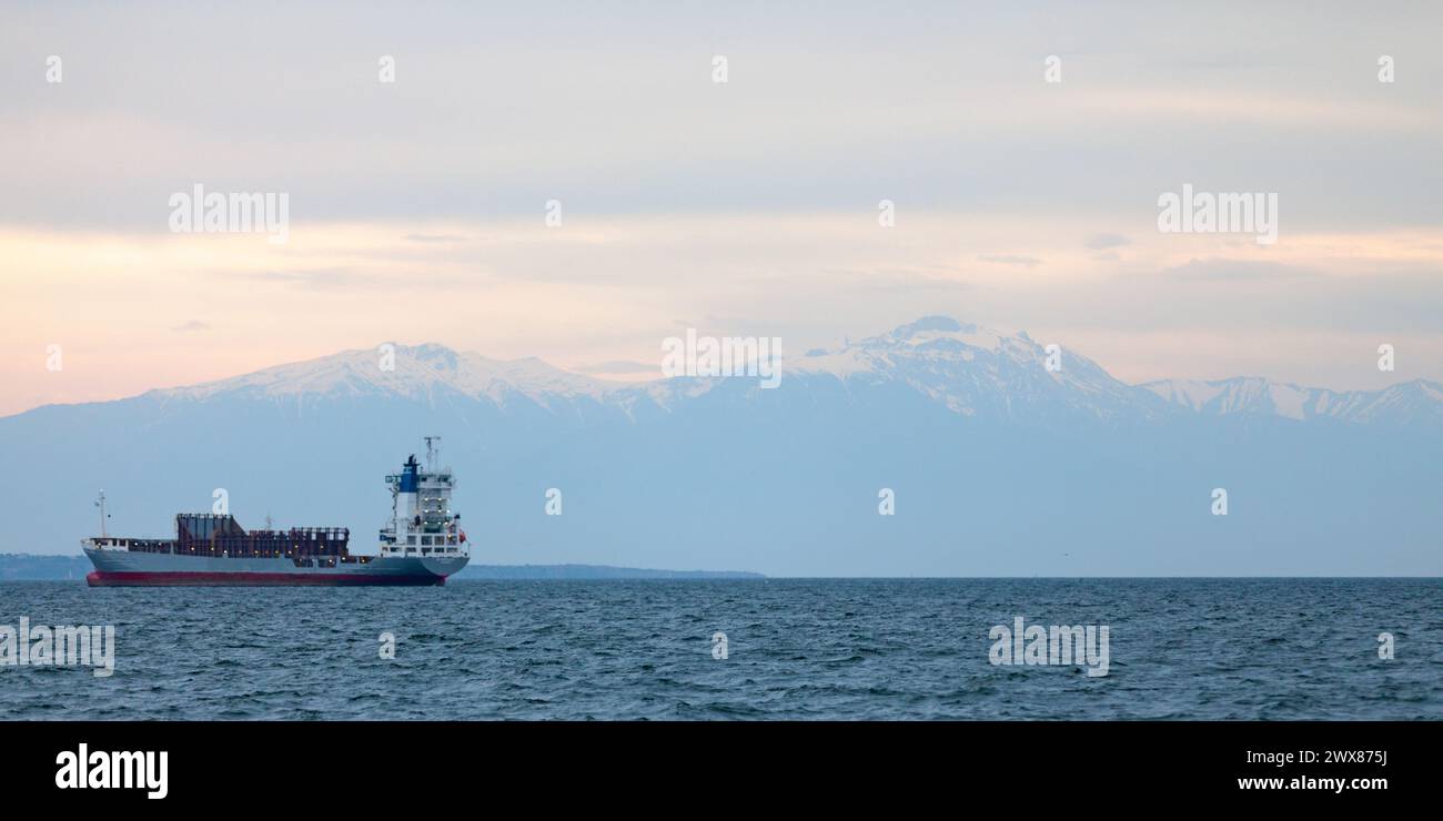 Thessaloniki, Griechenland - 03. Mai 2019: Frachtschiffe im Thermaischen Golf vor dem schneebedeckten Gipfel des Olymp bei Sonnenuntergang vor Anker. Stockfoto