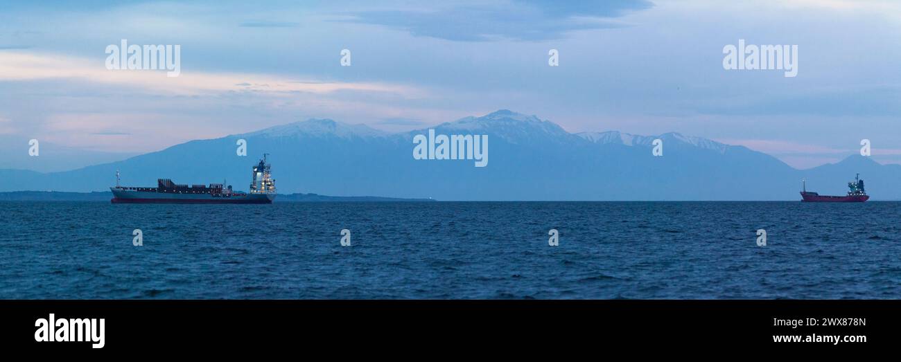 Thessaloniki, Griechenland - 03. Mai 2019: Frachtschiffe in der Bucht von Thessaloniki vor Anker vor dem schneebedeckten Gipfel des Olymp bei Sonnenaufgang Stockfoto
