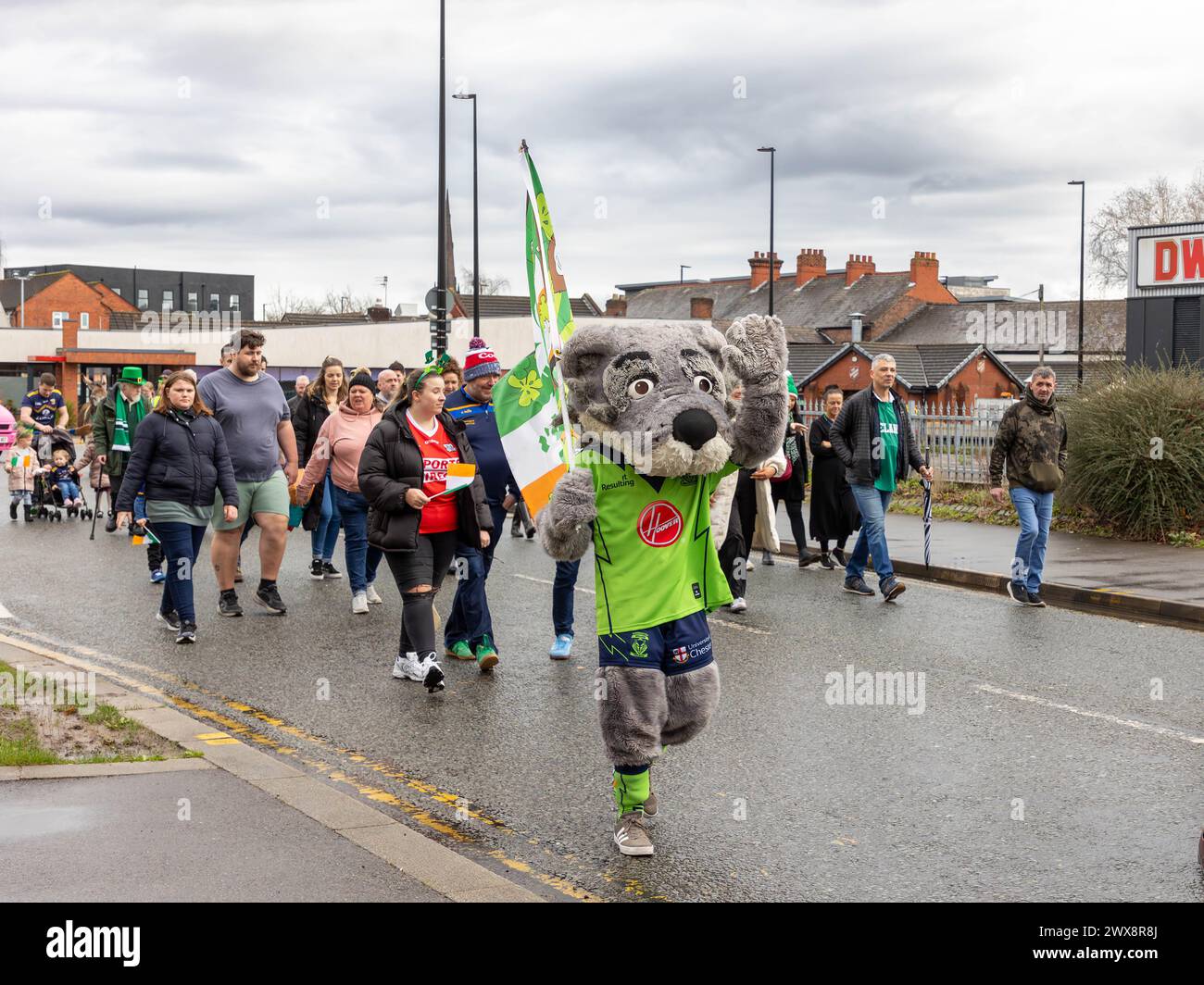 Warrington Rugby League Mascot, Wolfie, weht beim Spaziergang in der St. Patrick's Day Parade 2024 Stockfoto