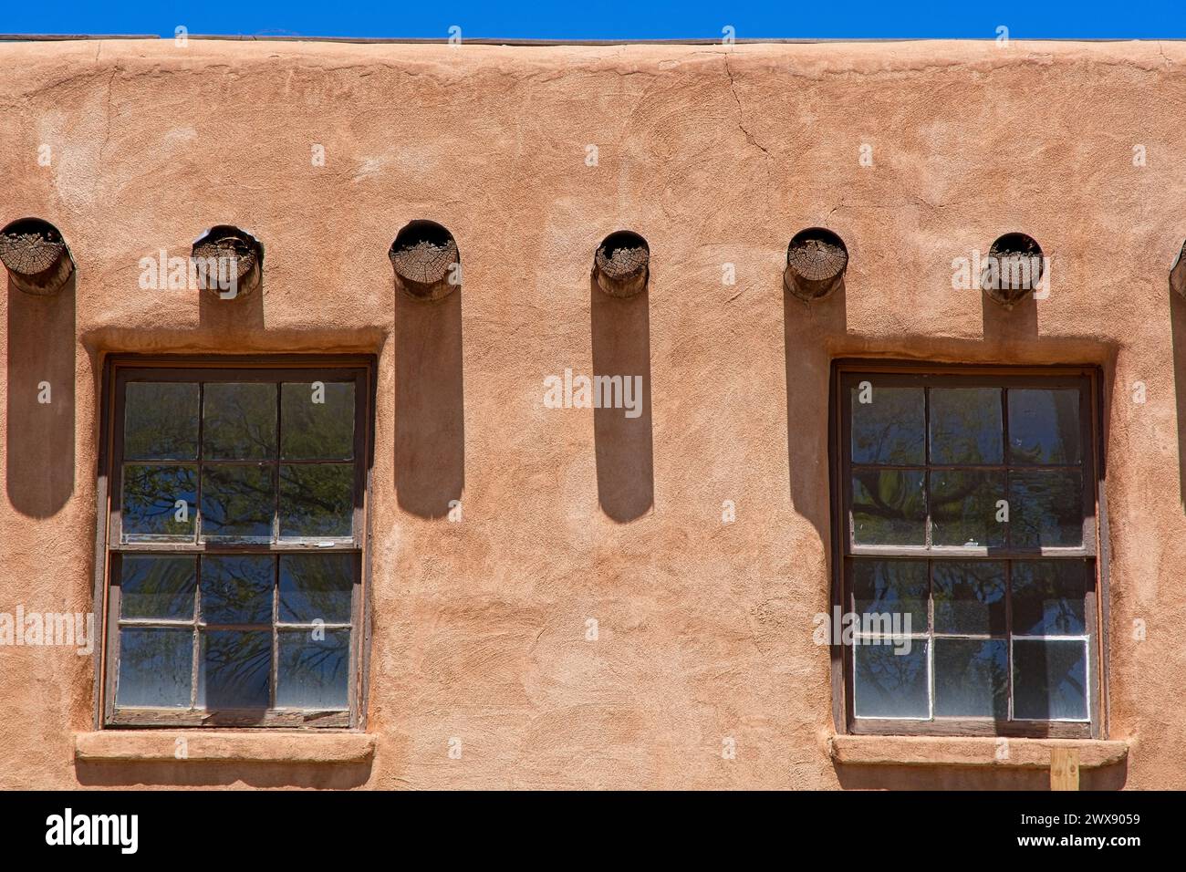 Schließen Sie rustikale Fenster unter einer Reihe freiliegender Viga-Dachbalken in einer Wand im lehmstil Stockfoto