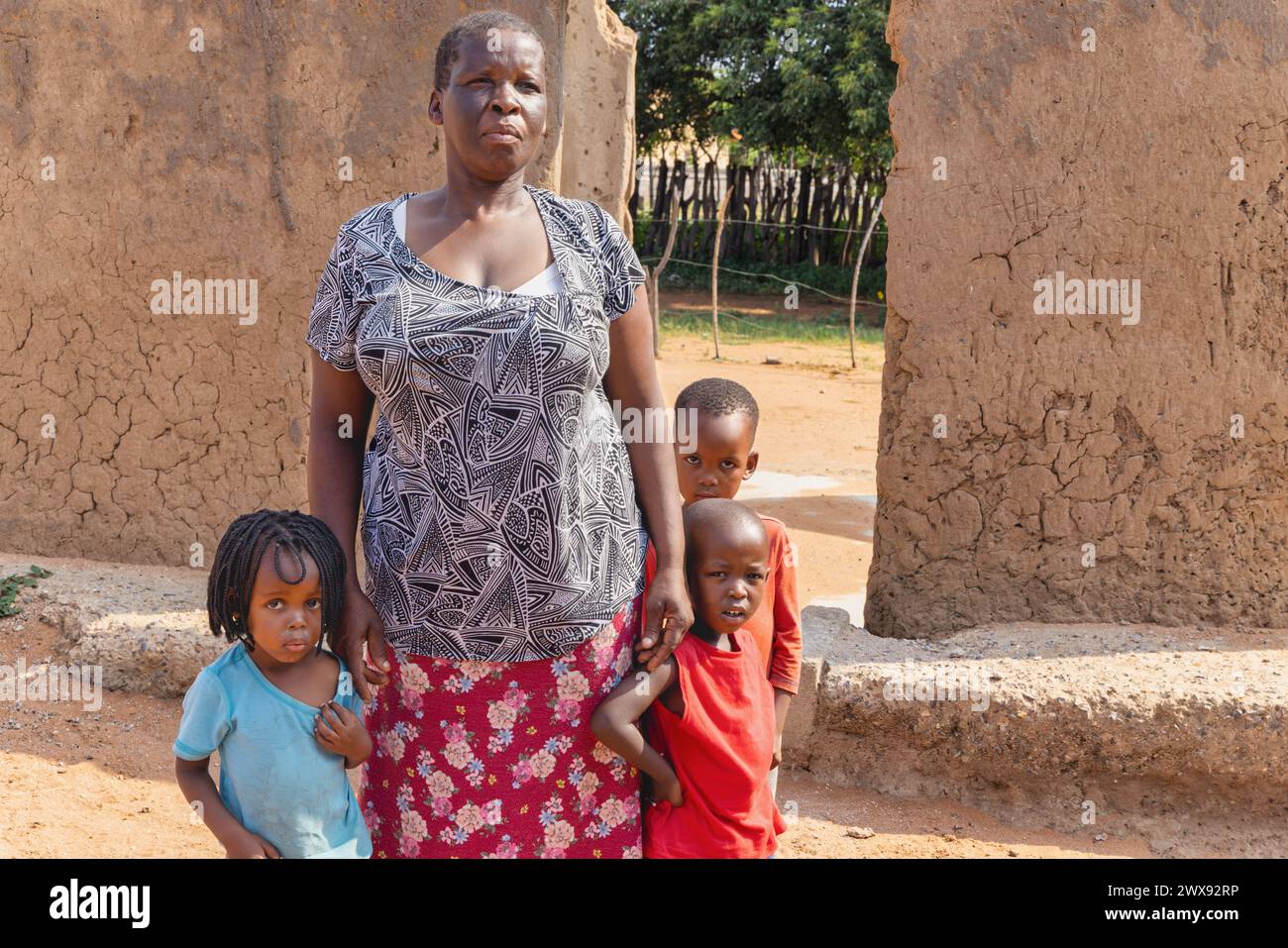 afrikanische Familie mit drei Kindern, die vor dem Lehmhaus stehen, afrikanisches Dorfleben Stockfoto
