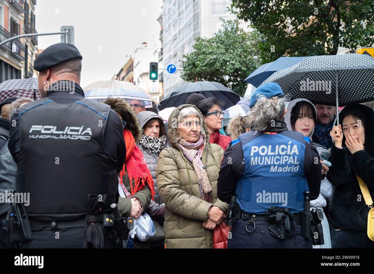 Madrid, Spanien. März 2024. Die Menschen warteten am Heiligen Donnerstag vor der Kirche San Isidro, auch bekannt als Stiftskirche San Isidore, unter dem Regen, da die Prozession unterbrochen wurde. Madrid erlebte ungünstige Wetterbedingungen, darunter Regen und Wind, was die Absage der Osterprozessionen am Donnerstag zwang. Diese Entscheidung wurde getroffen, um Verletzungen von Pönitenten durch rutschige Böden zu verhindern und die unbezahlbare Geschichte und das Erbe der Bruderschaften zu bewahren. Quelle: SOPA Images Limited/Alamy Live News Stockfoto