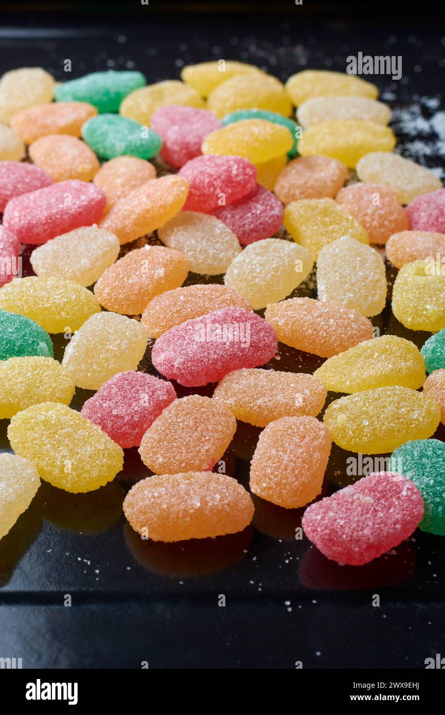 jujubes, bunte gummiartige Bonbons mit Fruchtgeschmack und länglich geformtem, verstreuten schwarzen Hintergrund, weicher Fokus mit Kopierraum Stockfoto