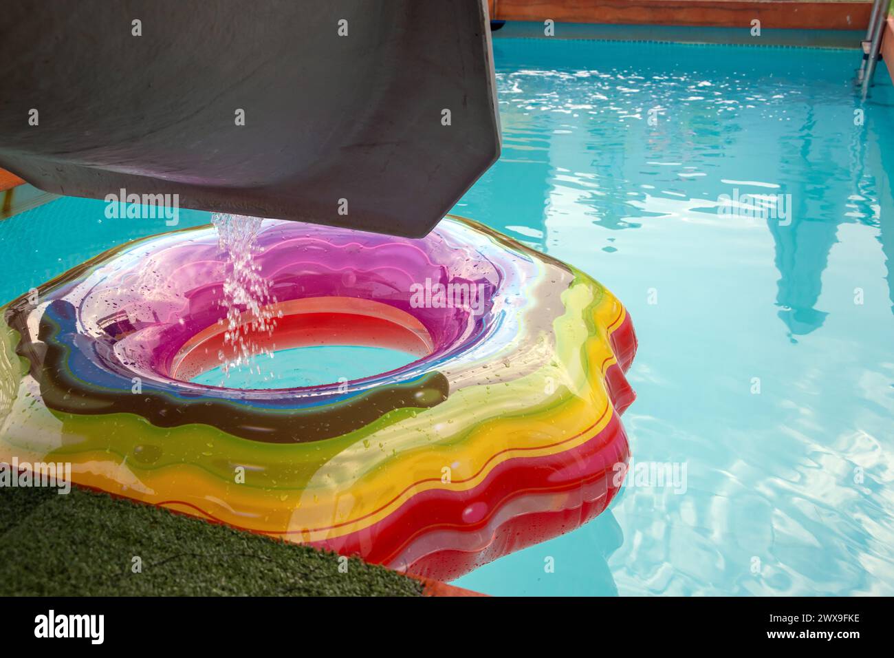 Wasser fließt von einer Rutsche in einen Pool, wo ein bunter aufblasbarer Ring schwimmt. Abends in einem leeren Swimmingpool Stockfoto