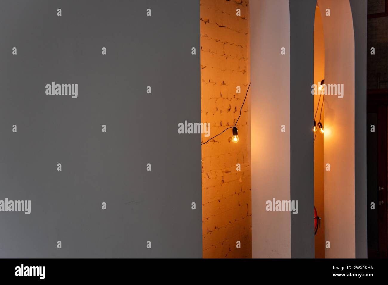 Lichterketten strahlen den strukturierten Ziegelstein in einem urbanen Loft warm aus und schaffen ein gemütliches und modernes Ambiente im minimalistischen Raum. Warmes Licht in U Stockfoto