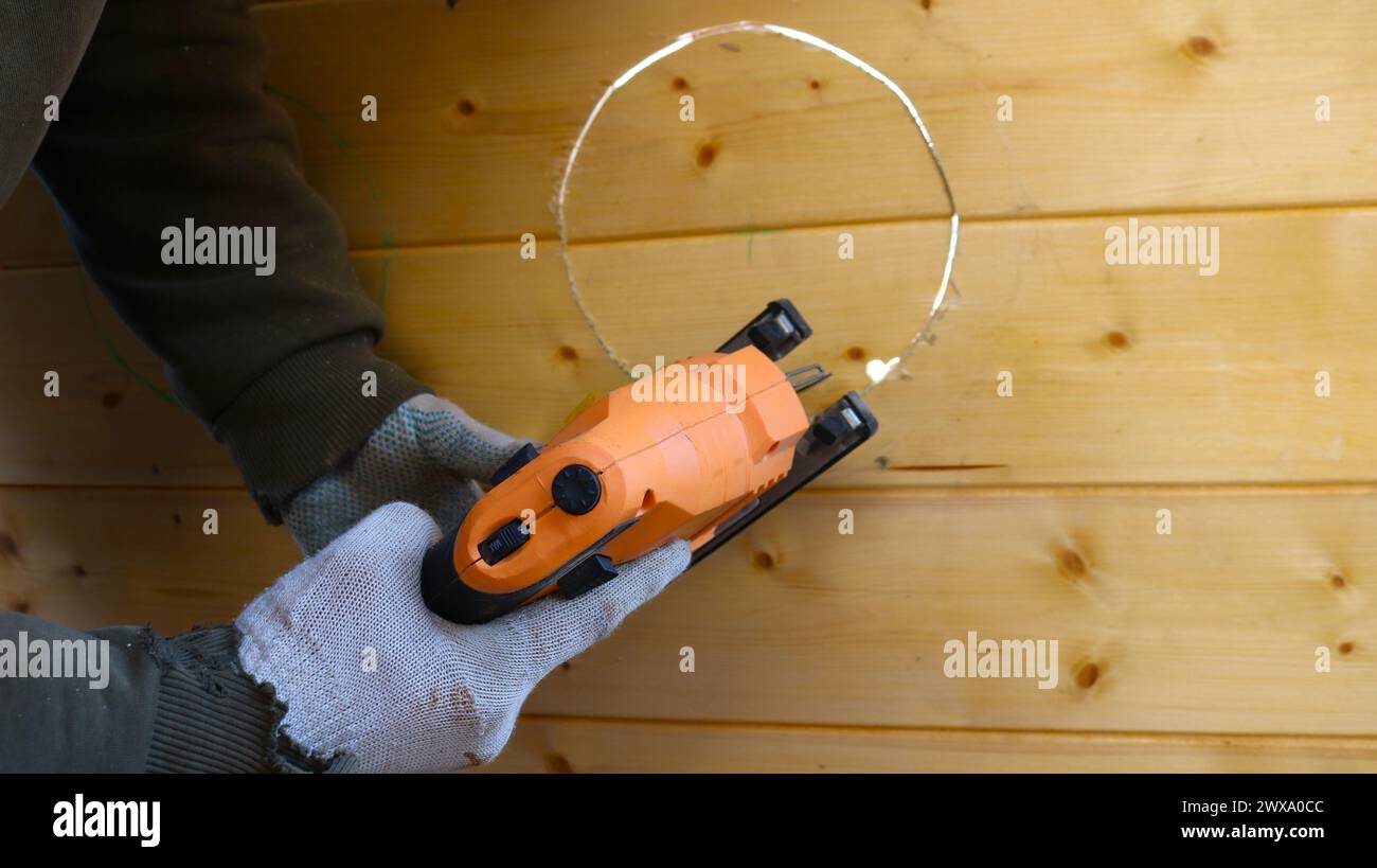 Arbeiten mit einer Stichsäge auf einer Holzoberfläche, Schneiden eines Kreises mit einer Stichsäge, ein funktionierendes Bauwerkzeug in männlichen Händen in Handschuhen Nahaufnahme während der Arbeit Stockfoto