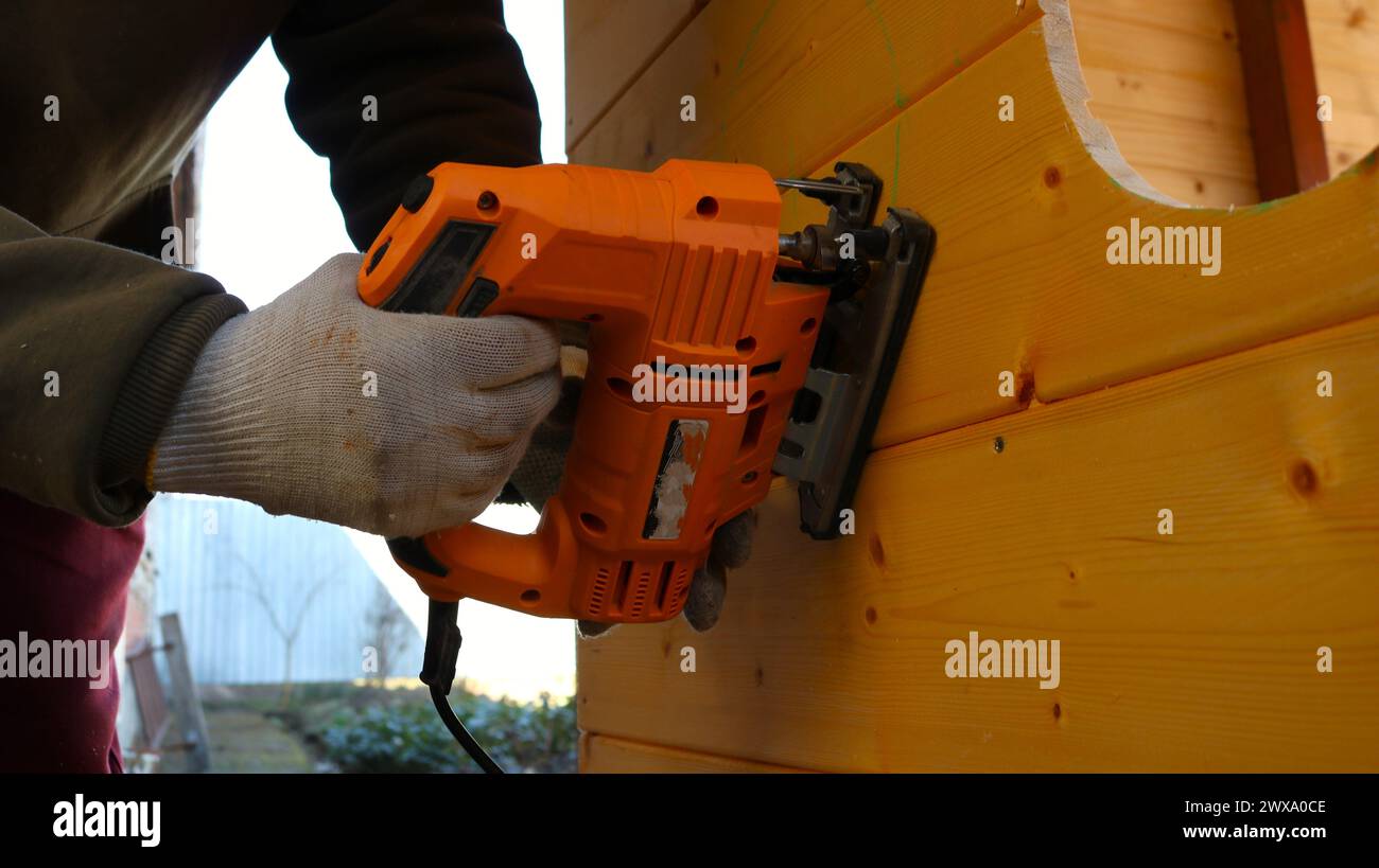 Arbeiten mit einer Stichsäge, um runde Löcher in eine Holzkonstruktion zu schneiden, die Hände eines Arbeiters mit einer elektrischen Maschine, um Kreise in einem Holz zu schneiden Stockfoto